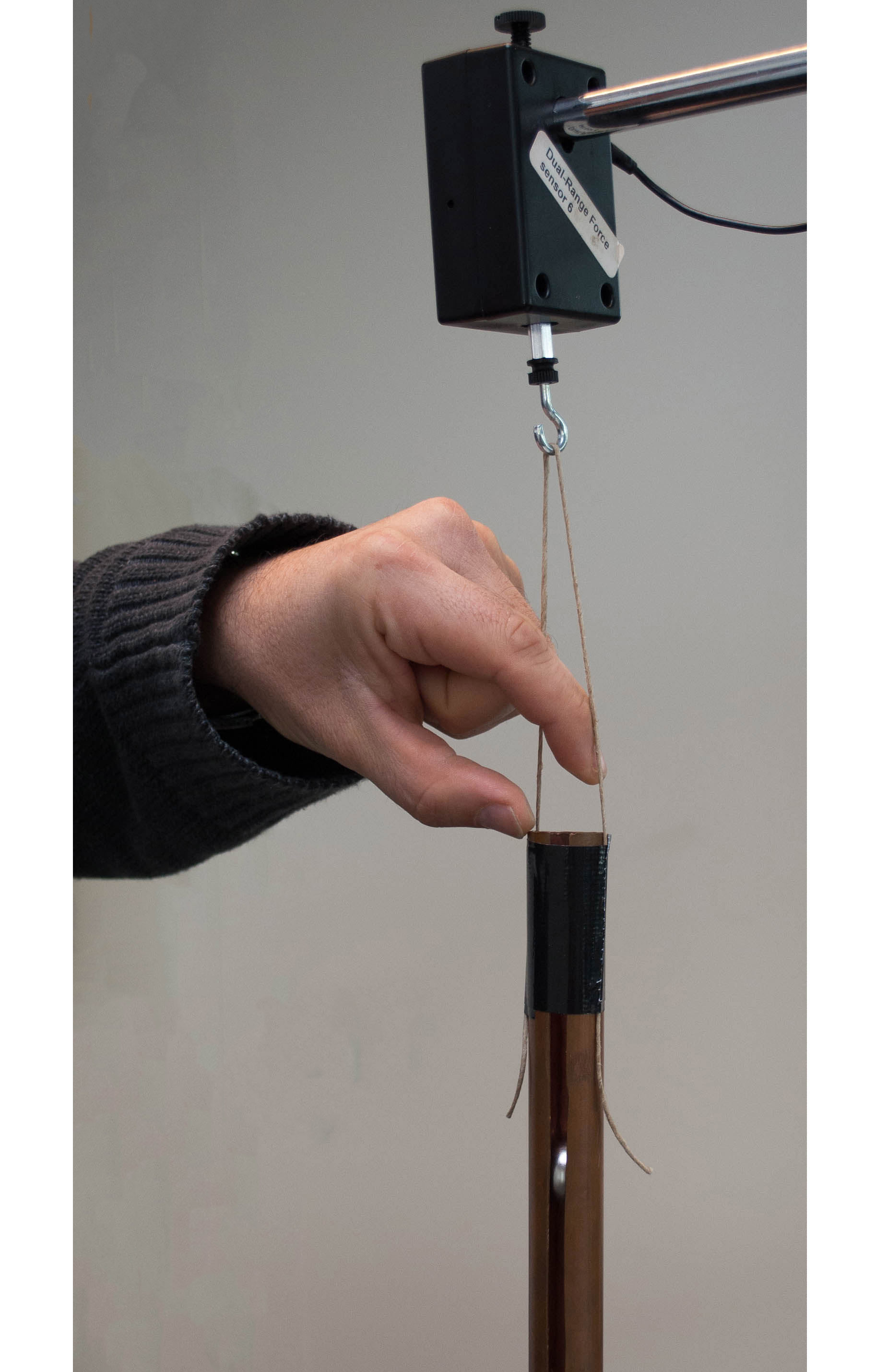a copper tube hanging on a digital scale. A hand, just released the magnet.