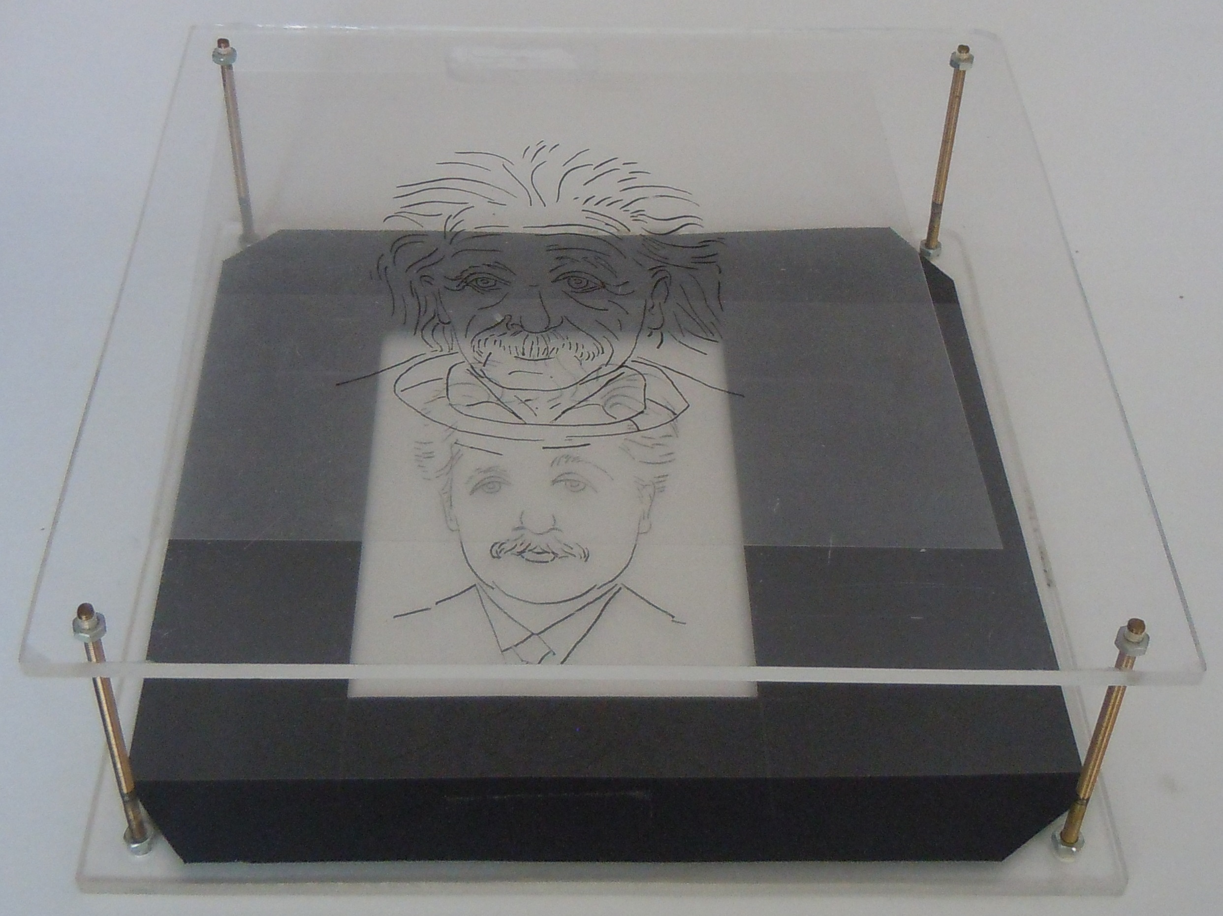 Box with transparant perspex. Both drawings of Einstein on transparant plate are visible.
