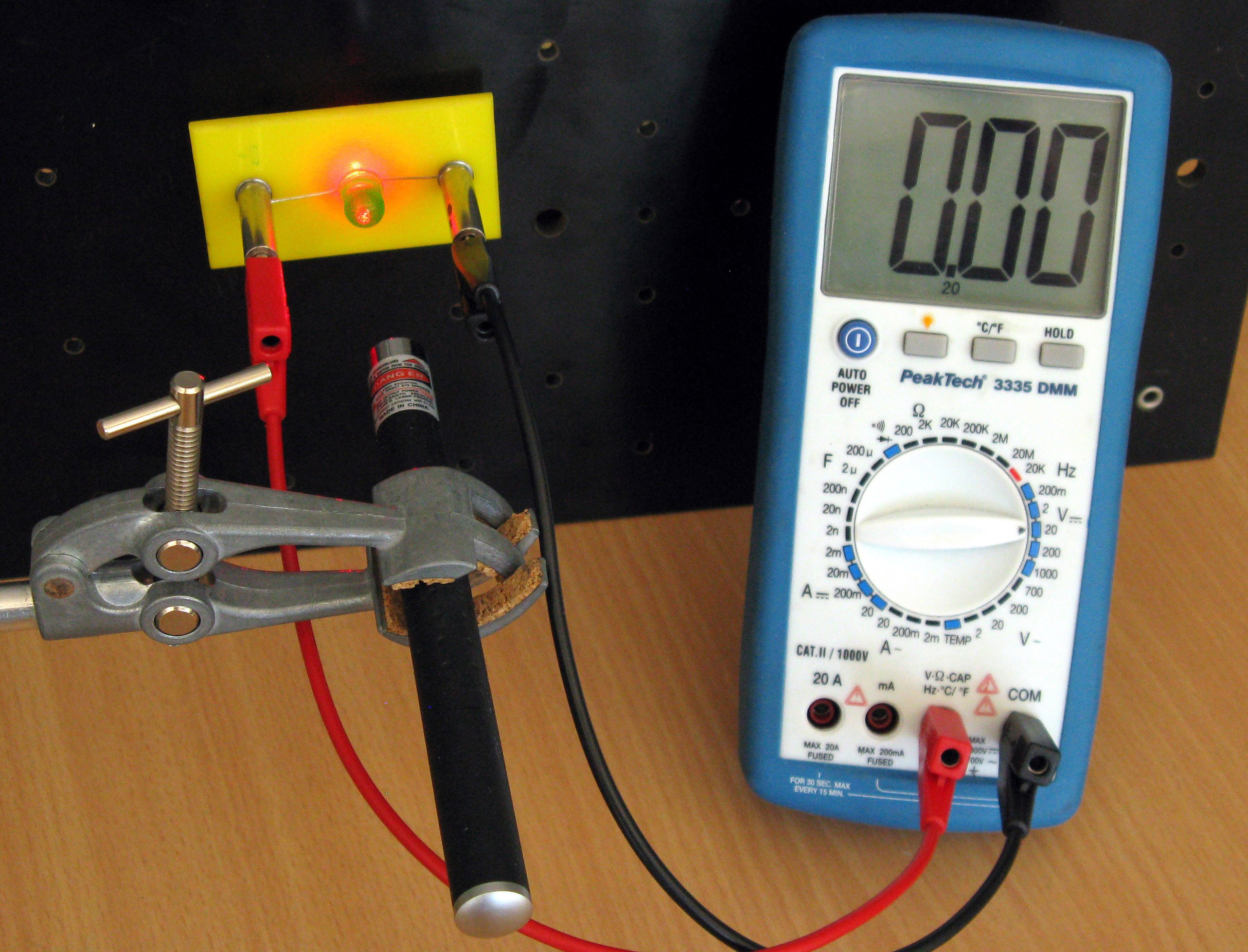 red laser shining on green led, led connected to digital multimeter indicating no voltage