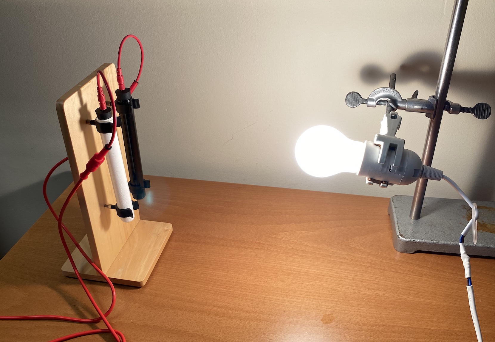 a light bulb shining near a black and a white tubes, a thermometer inserted in the tubes.