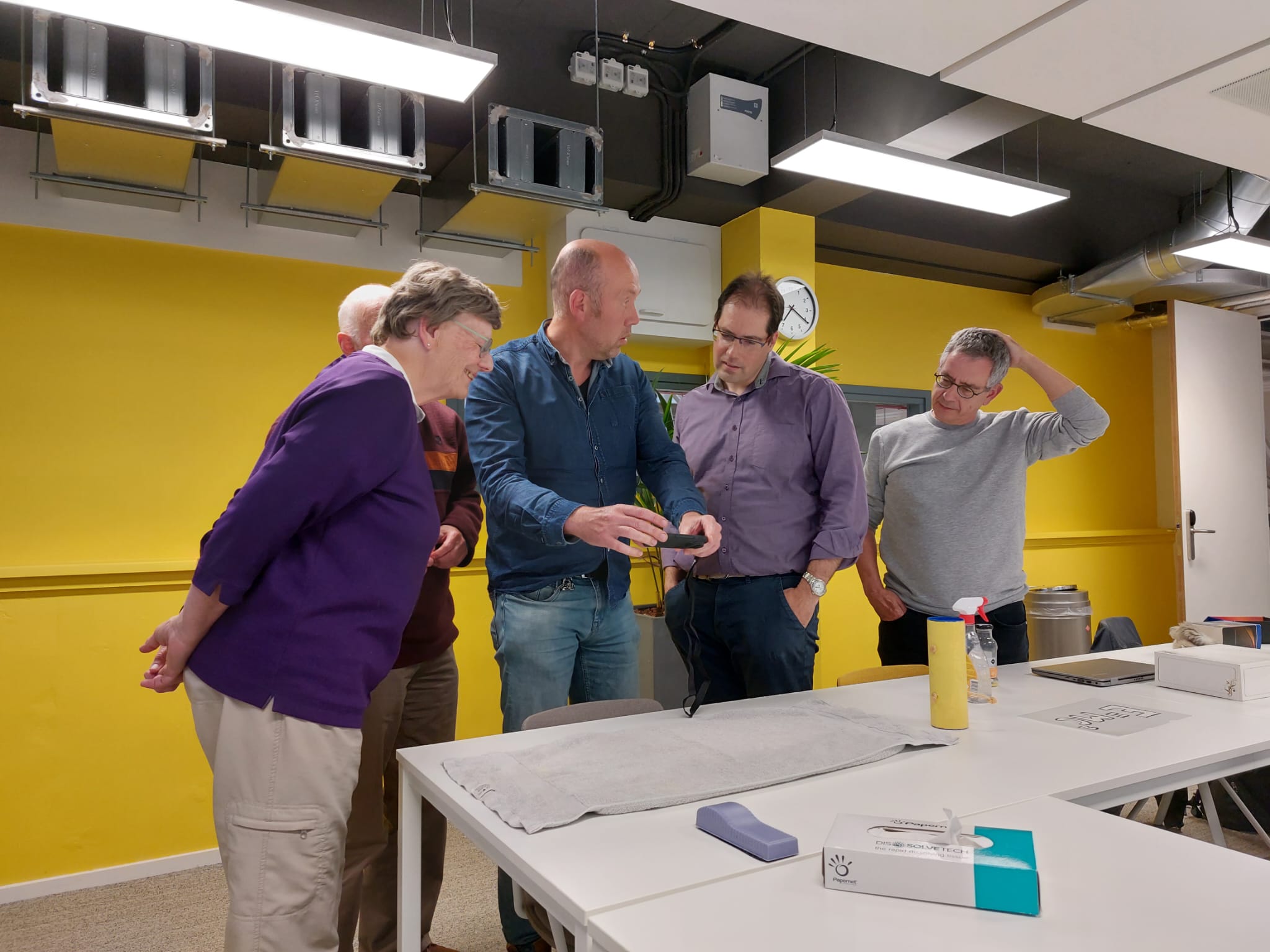 part of the author team standing around a table where one of the authors demonstrate a demonstration.